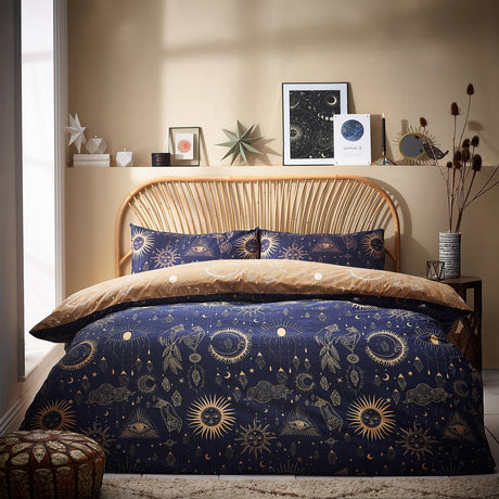 Constellation Printed Reversible Duvet Cover Set in gold/navy on a rattan bed, navy side with gold sun, moon and star motifs shown with matching pillowcases in a bedroom setting.