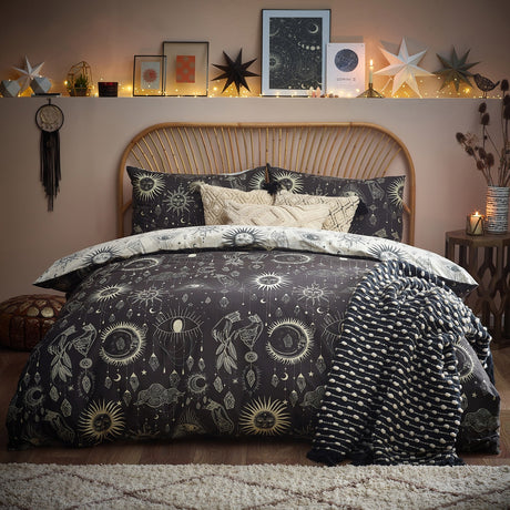 Constellation Printed Reversible Duvet Cover Set on a bed with rattan headboard, charcoal ground with cream sun, moon and star motifs, styled with a monochrome patterned throw.
