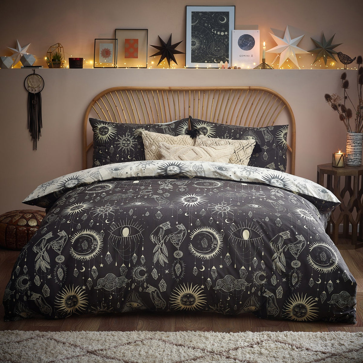 Constellation Printed Reversible Duvet Cover Set in Multi, shown on a bed with charcoal side facing up, printed with cream suns, moons, stars and hanging jewels, styled in a bohemian bedroom.