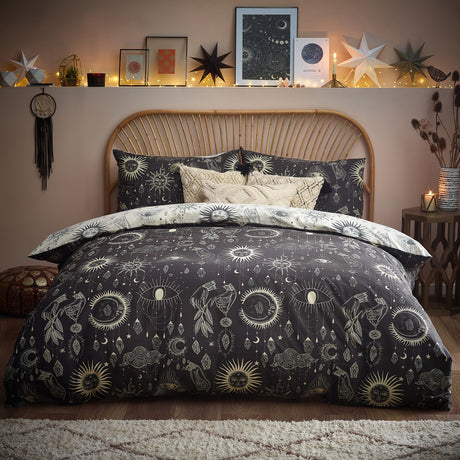 Constellation Printed Reversible Duvet Cover Set in Multi, shown on a bed with charcoal side facing up, printed with cream suns, moons, stars and hanging jewels, styled in a bohemian bedroom.