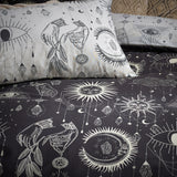 Constellation Printed Reversible Duvet Cover Set in Multi, shown on bedding with charcoal and cream sides featuring suns, moons, stars, eyes and hanging jewel motifs.