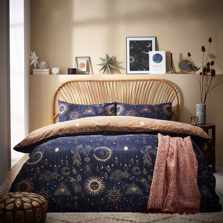 Constellation Printed Reversible Duvet Cover Set in gold and navy on a bed with matching pillowcases, shown in a bedroom with rattan headboard and shelf decor.
