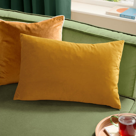 Contra Velvet Linen Cushion in mustard, an oblong velvet-fronted cushion shown on a green sofa alongside a matching square cushion.