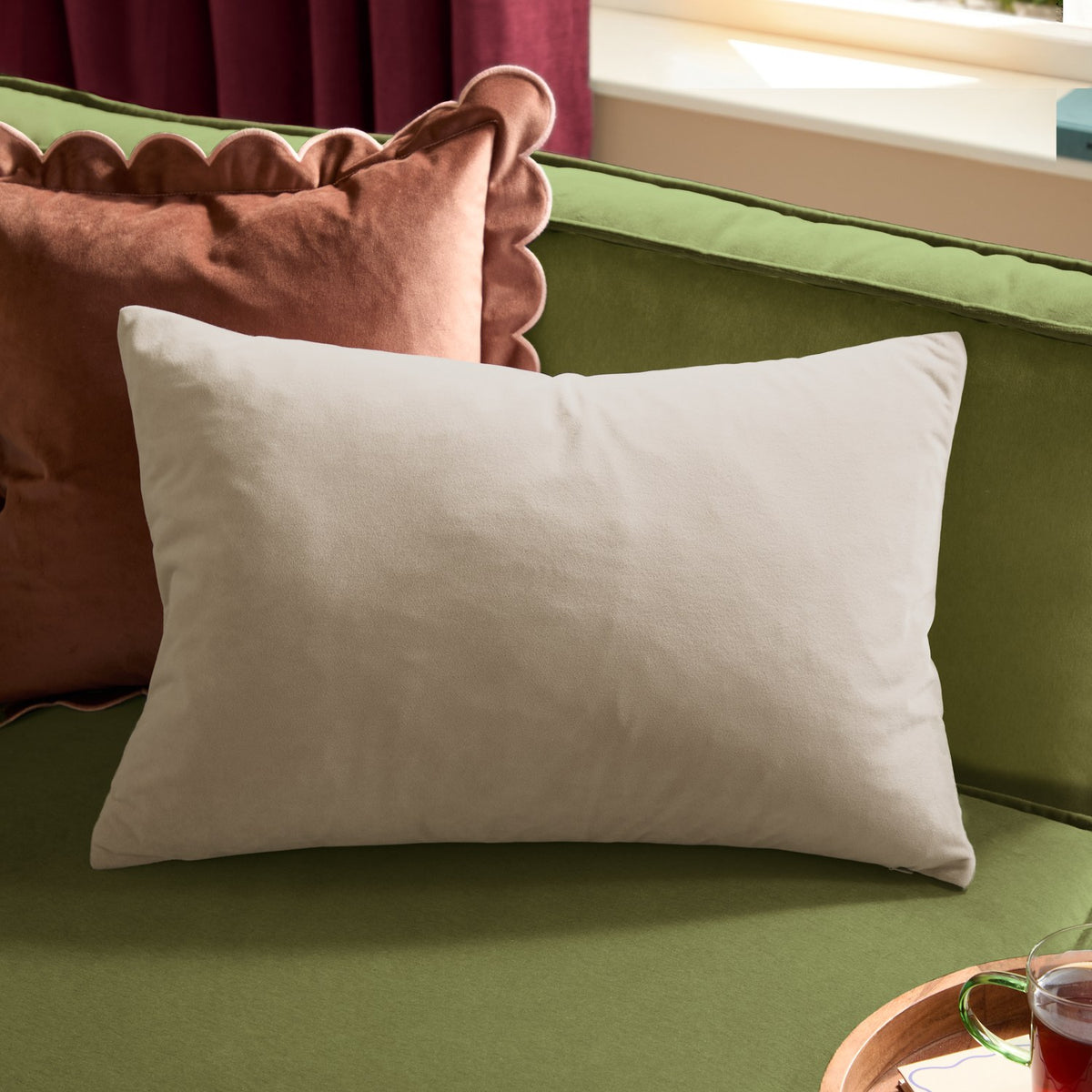 Contra Velvet Linen Cushion in natural, rectangular velvet-faced cushion shown on a green sofa alongside a scalloped rust-coloured velvet cushion.