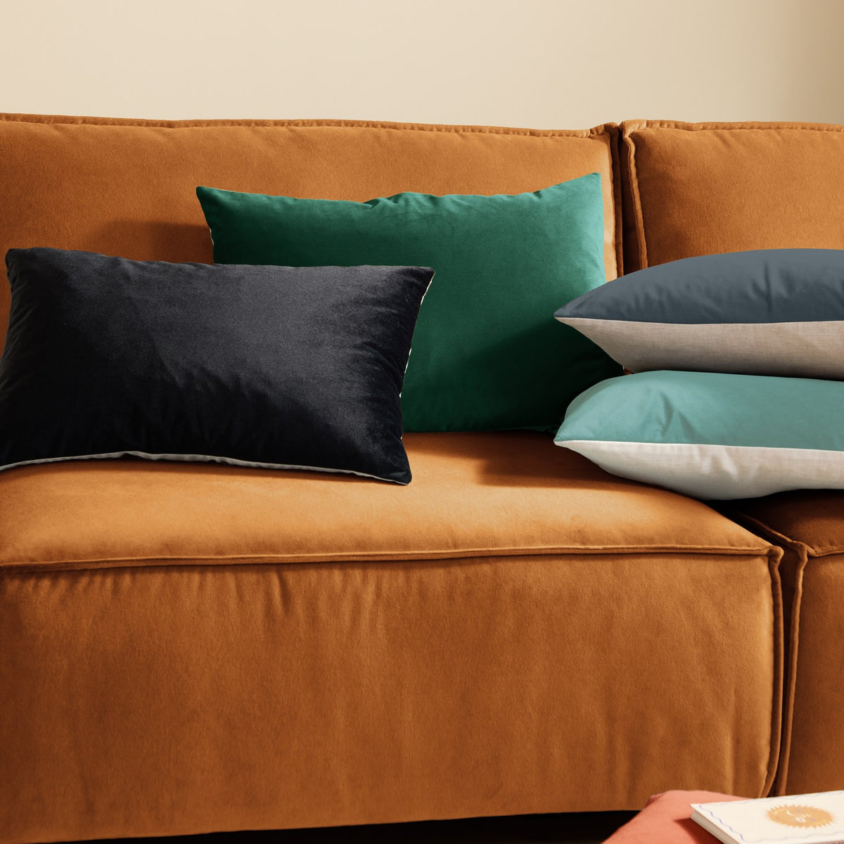 Contra Velvet Linen Cushion in teal, rectangular velvet cushion shown on a burnt orange velvet sofa alongside black, grey and white cushions.