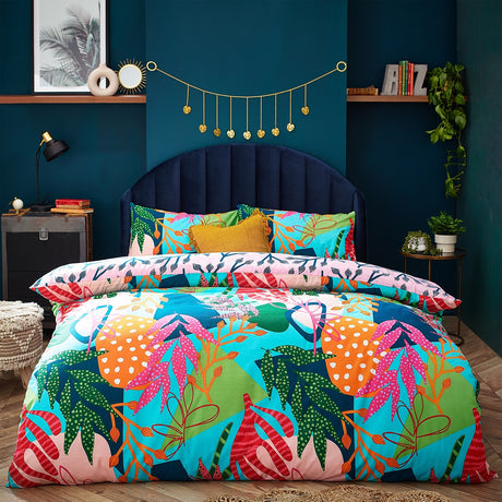 Coralina Jungle Floral Duvet Cover Set in multicoloured tropical print with pink, orange, green and navy leaf motifs, shown on a bed with matching pillowcases and a mustard cushion in a teal bedroom.