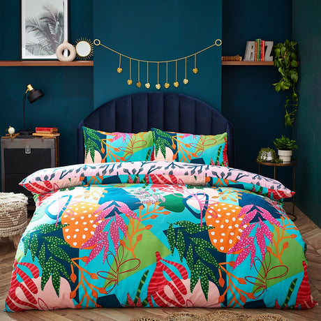 Coralina Jungle Floral Duvet Cover Set in multicoloured tropical print with pink, orange, green and navy leaves, shown on a bed with matching pillowcases in a dark teal bedroom.