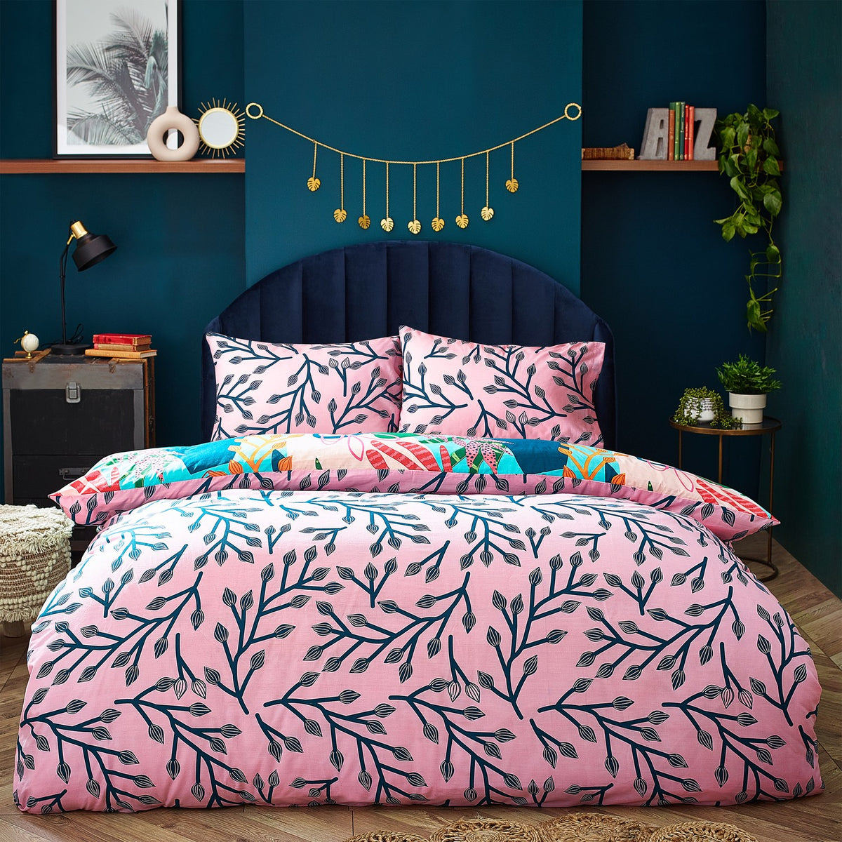 Coralina Jungle Floral Duvet Cover Set shown reversed, with a pink ground and navy branching leaf print, styled on a bed with matching pillowcases in a teal bedroom.