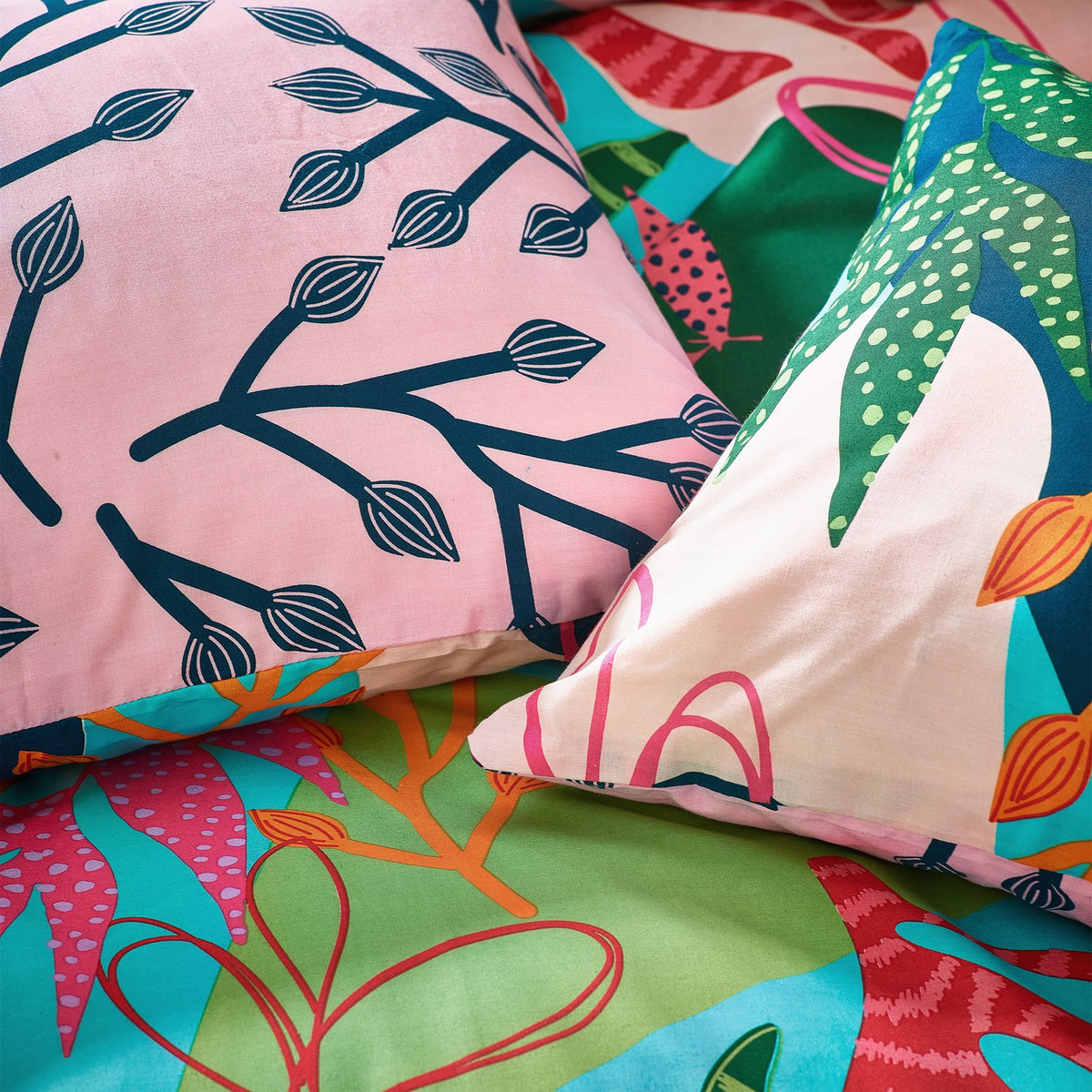 Coralina Jungle Floral Duvet Cover Set showing pink navy branching leaf reverse alongside tropical multicoloured leaf and seed pod print in pink, orange, green and teal.