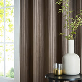 Corinthian Velvet Lined Eyelet Curtains in taupe, showing fine micro-pleated velvet fabric with vertical ridges, hung beside a window in a living room setting with a side table, vase, and greenery.