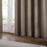 Corinthian Velvet Lined Eyelet Curtains in taupe, showing fine micro-pleated velvet fabric pooling on a wooden floor beside a glazed door in a living room setting.