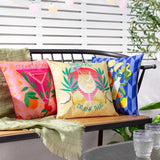 Cosmo O' Clock square cushion in pink polyester with cocktail glass print, oranges and berries, styled on an outdoor bench beside coordinating printed cushions.