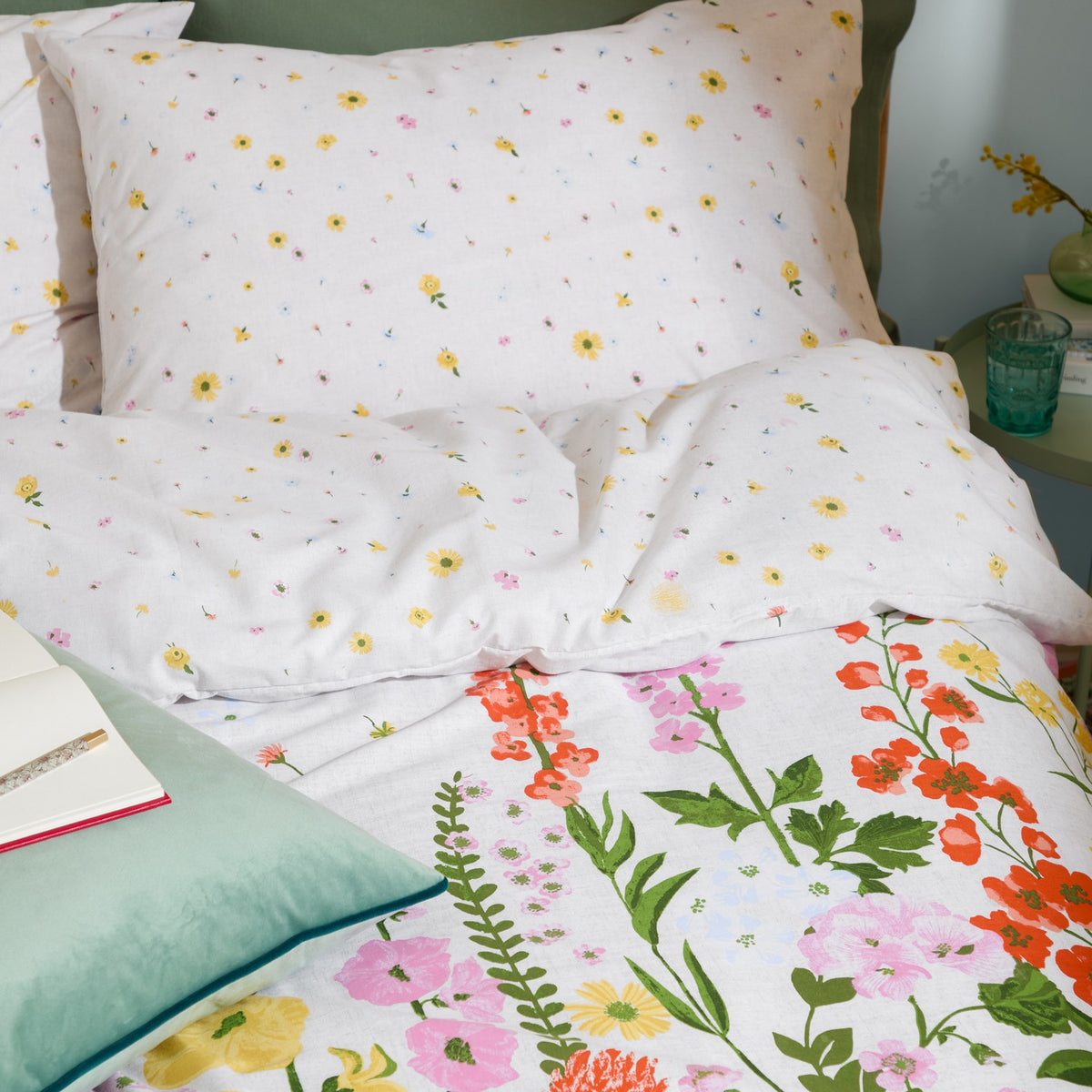 Cottage Garden Reversible Ditsy Duvet Cover Set on a bedroom bed, showing the ditsy floral pillowcases and the reverse side's climbing pink, coral and yellow floral border.