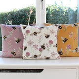 Country Animal Velvet Cushion in heather pink with bumblebee and clover print, shown on a windowsill beside cream and mustard bee-print cushions.
