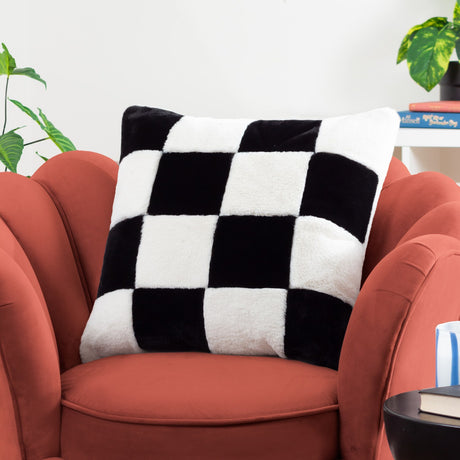 Cozee Check faux fur square cushion in black and white checkerboard, shown on a rust-coloured armchair in a living room setting.