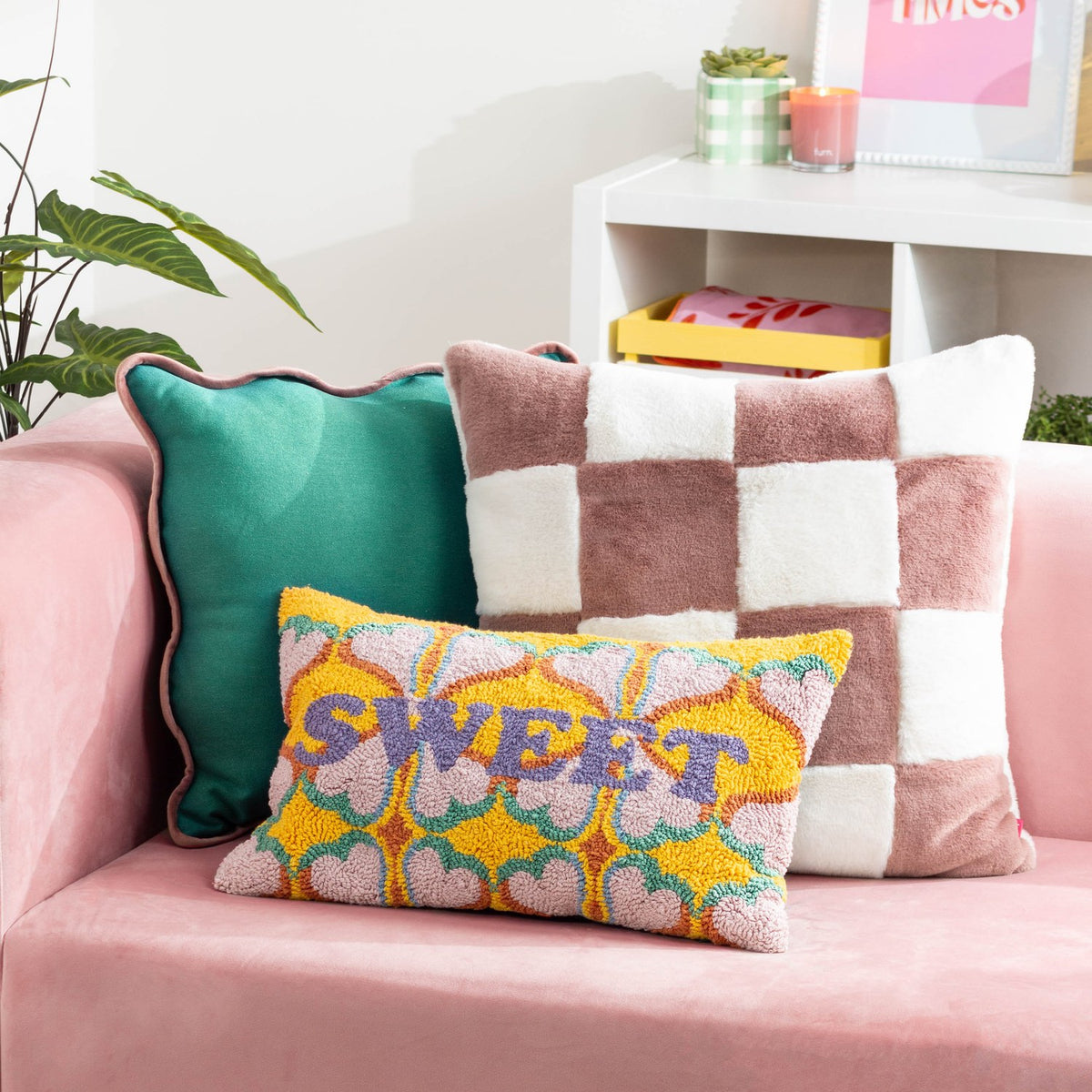 Cozee Check Plain Faux Fur Cushion in pink and cream checkerboard, 50 x 50cm, shown on a pink sofa with a teal cushion and patterned lumbar cushion.