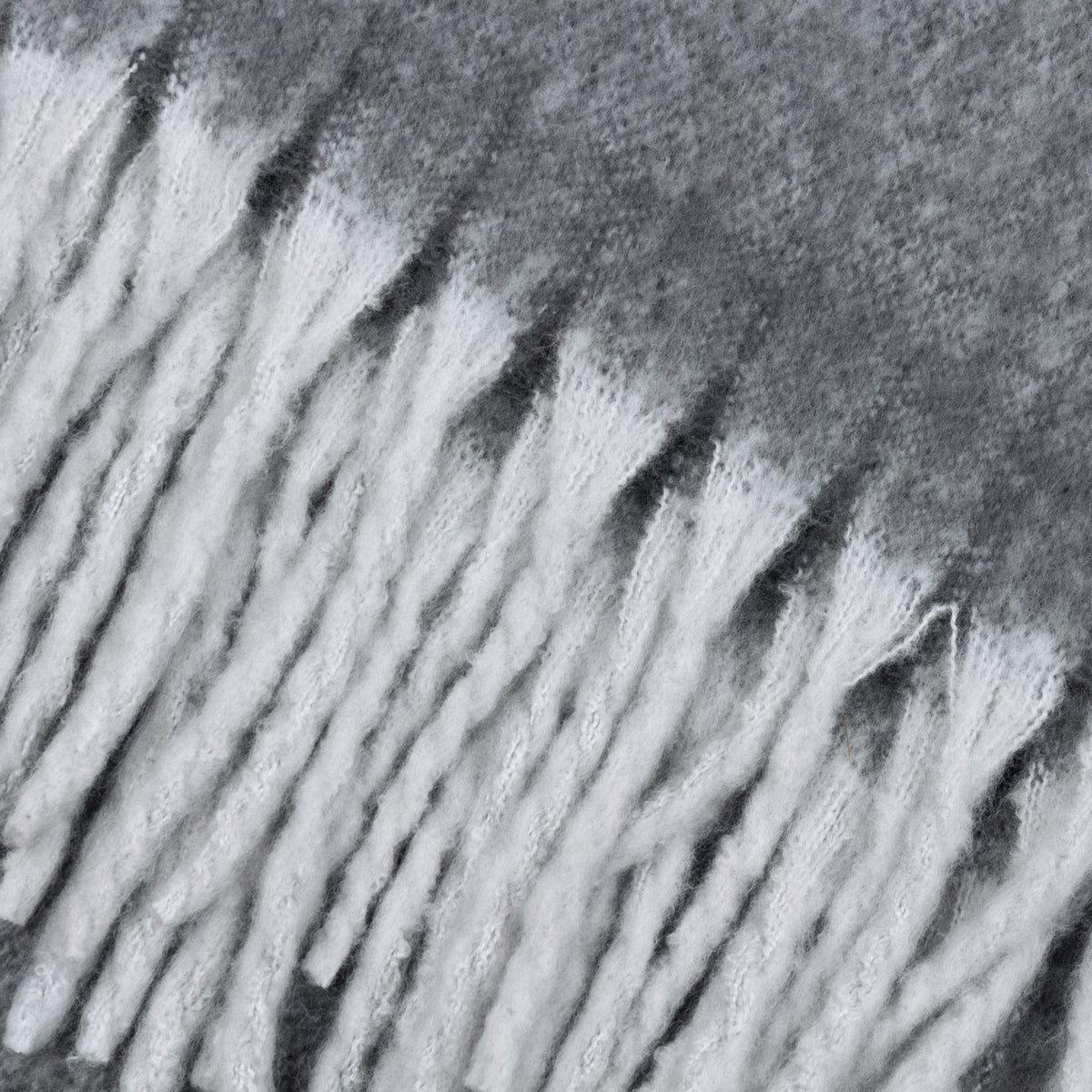 Close-up of the Cosy Plain Polyester Throw in charcoal grey, showing the woven texture and deep white tasselled fringe along the edge.