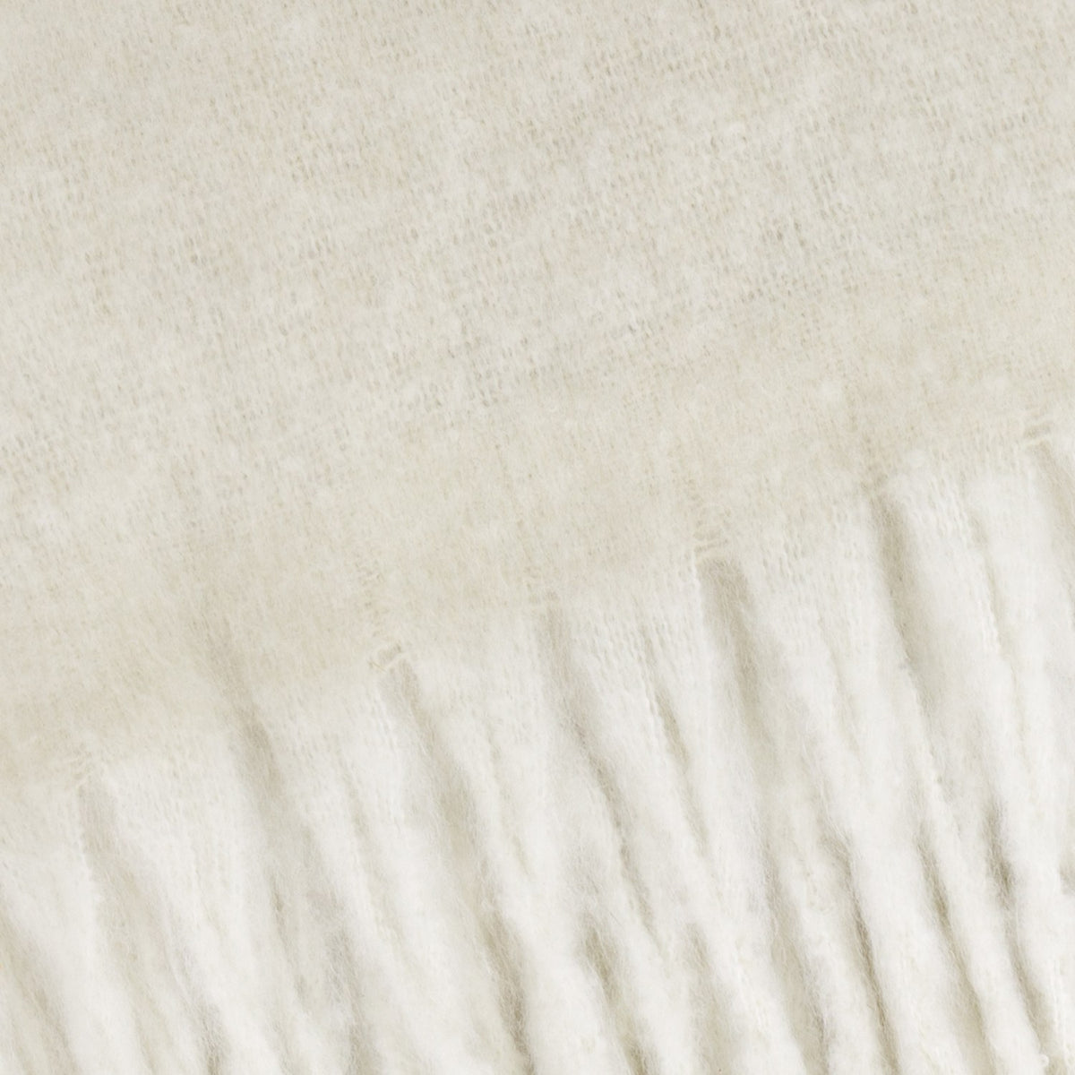 Close-up of the Cosy Plain Polyester Throw in ecru, showing the brushed woven surface transitioning into a knotted fringe edge in cream tones.
