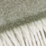Close-up of the Cosy Plain Polyester Throw in green, showing the woven sage-grey body meeting a chunky ivory fringed trim.