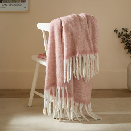 Cosy Plain Polyester Throw in blush pink with chunky ivory fringe, draped over a white chair in a living room setting.