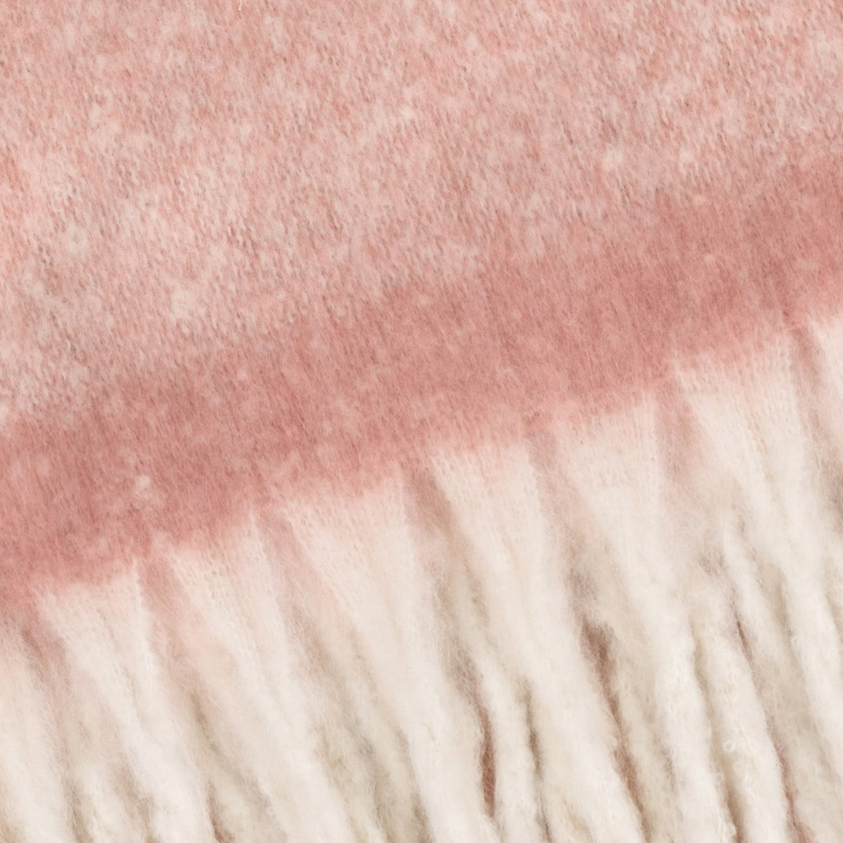 Close-up of the Cosy Plain Polyester Throw in pink, showing the brushed, textured fabric fading to cream with a chunky ivory fringe edge.
