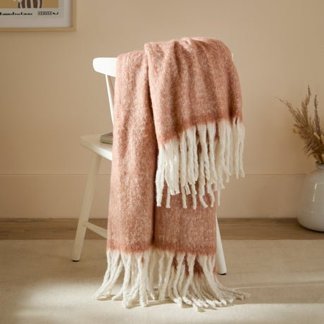 Cosy Plain Polyester Throw in rust with cream knotted fringe, draped over a white chair in a living room setting.