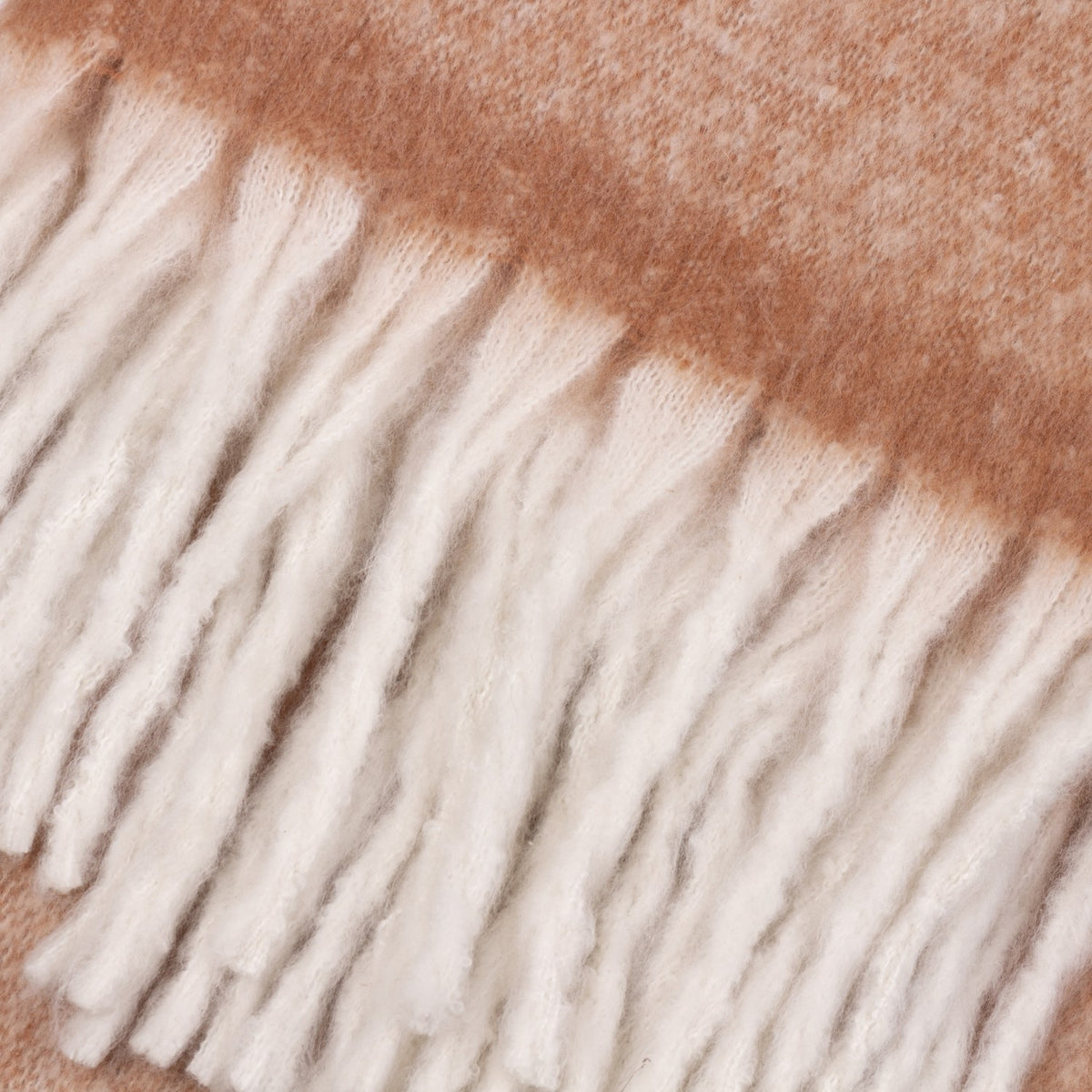 Close-up of the Cosy Plain Polyester Throw in rust, showing the woven fabric edge and loose cream knotted fringe tassels.