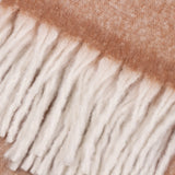 Close-up of the Cosy Plain Polyester Throw in rust, showing the woven fabric edge and loose cream knotted fringe tassels.