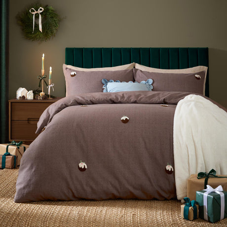 Chocolate-brown brushed cotton duvet cover set with tufted Christmas pudding motifs on a herringbone ground, styled on a bed with a pale blue ruffled cushion in a bedroom with festive decor.