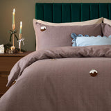 Chocolate-brown brushed cotton duvet cover set with tufted Christmas pudding motifs, styled on a bed with a teal headboard, blue cushions and bedside candles.