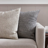 Croft Plain Velvet Cushion in charcoal, square with a woven chevron front in charcoal and cream, shown on a beige sofa beside a cream herringbone cushion.
