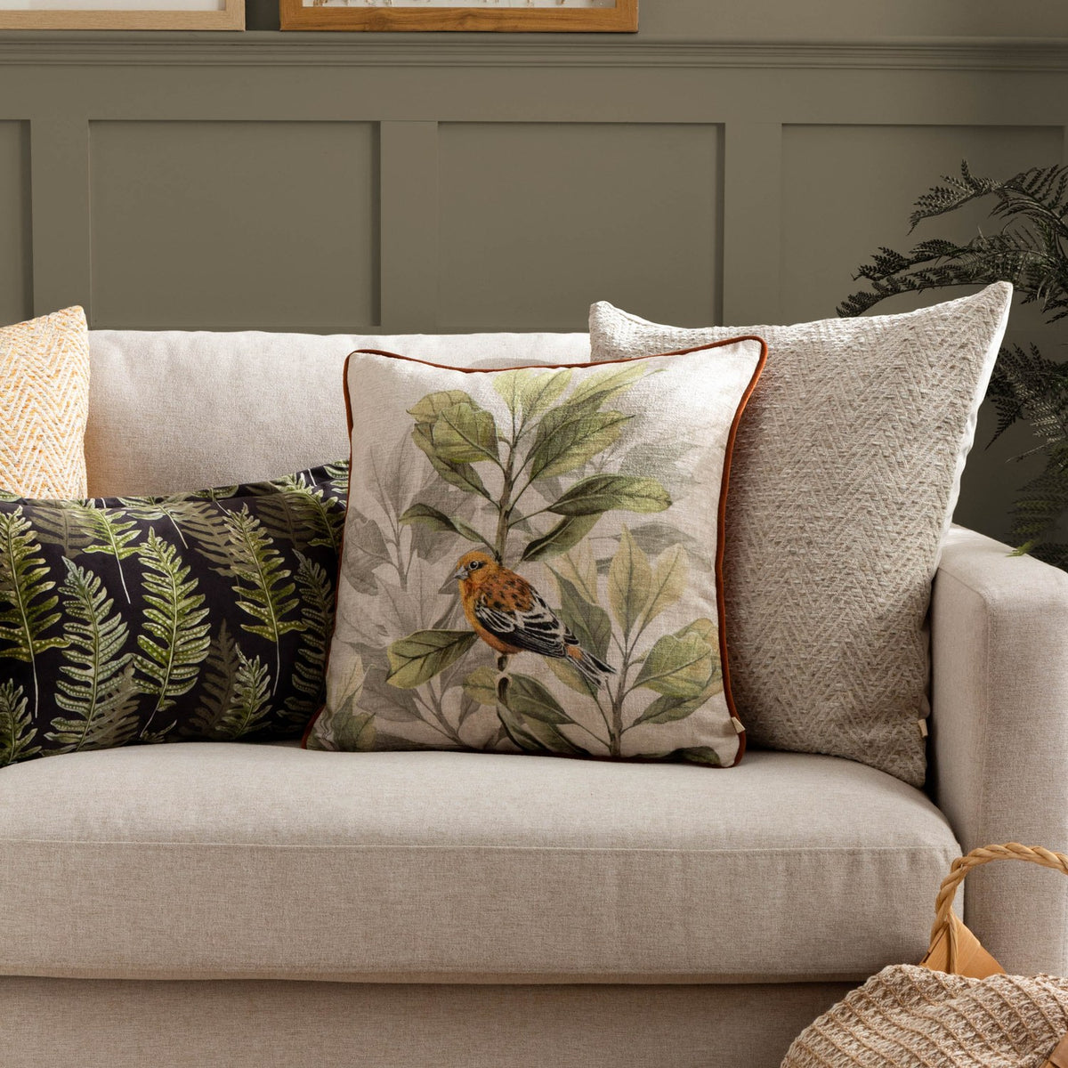 Croft Plain Velvet Cushion in natural oatmeal chevron twill, shown centred on a beige sofa alongside patterned and printed accent cushions in a living room setting.