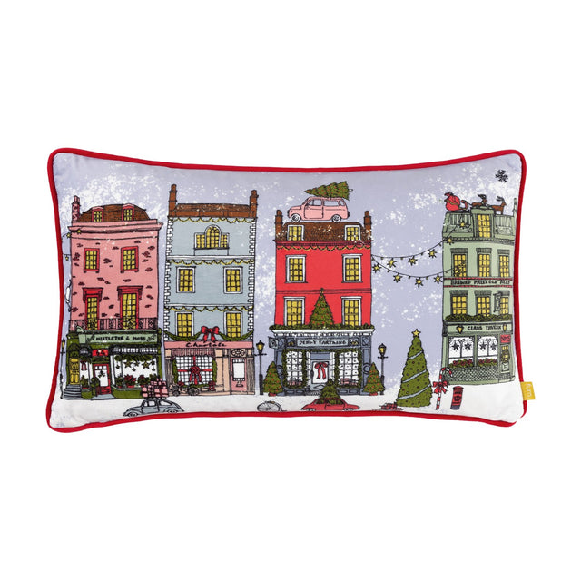 Christmas Spirit rectangular velvet cushion in multicolour, printed with a festive townhouse street scene, red piped edges, on a plain white background.