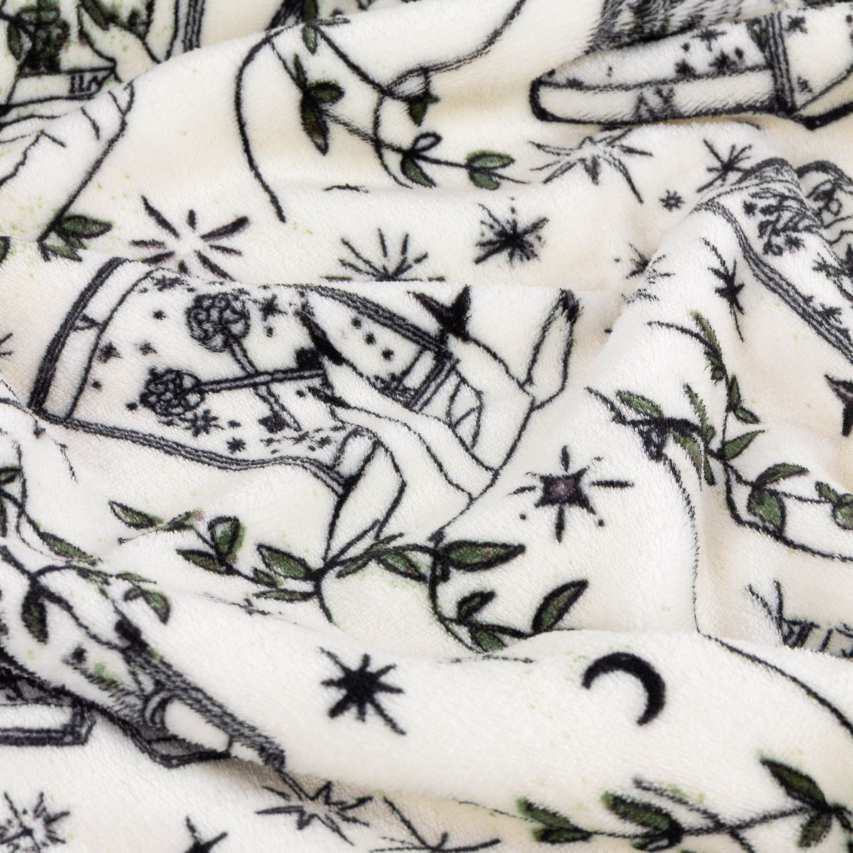 Celestial Stories printed polyester throw in cream, shown draped in folds with charcoal tarot card, hand, star, moon and green foliage motifs.