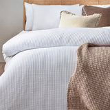 White Chunky Waffle Cotton Duvet Cover Set on a bed with matching pillowcases, styled with cream and brown cushions and a waffle-textured throw.