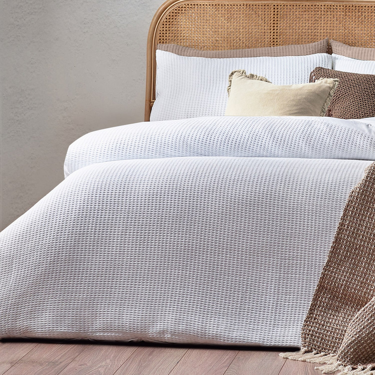 Chunky Waffle Cotton Duvet Cover Set in white on a bed with a rattan headboard, cream and brown cushions, and a woven throw.