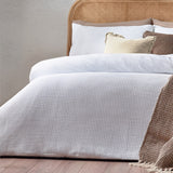 Chunky Waffle Cotton Duvet Cover Set in white on a bed with a rattan headboard, cream and brown cushions, and a woven throw.