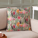 Country Wilds Blossom Floral polyester cushion in cream with pink, yellow and red florals and green foliage, piped edge, shown on a beige sofa.