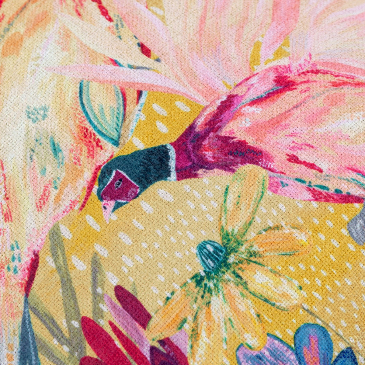 Close-up of the Country Wilds Pheasant Bloom cushion in gold, showing a hand-painted pheasant in flight with pink and coral tones, cream feathering and wildflower detail on polyester fabric.