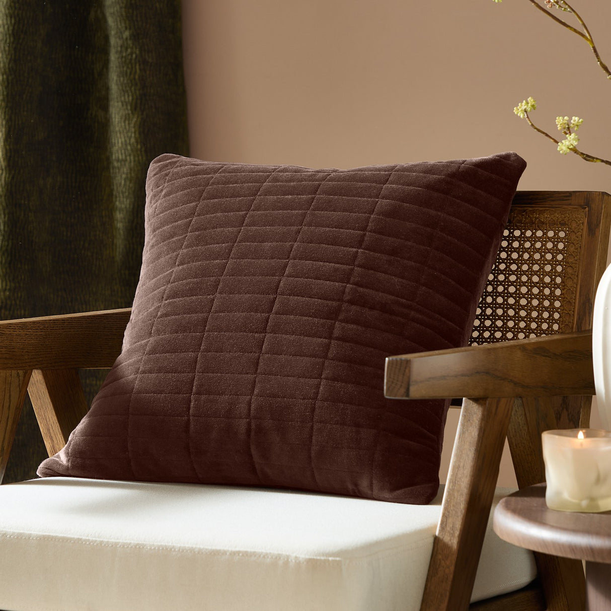 Dales quilted velvet cotton cushion in brown with a square shape, shown on a wooden armchair in a living room setting.