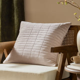 Dales Quilted Velvet Cotton Cushion in natural beige with a stitched grid pattern, shown on a wooden armchair in a living room setting.