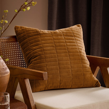 Dales Quilted Velvet Cotton Cushion in pecan brown, featuring a grid-stitched channel design, styled on a wooden armchair with cream cushioning.