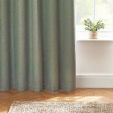 Dawn Plain Reversible Eyelet Curtains in Eucalyptus, dusty green marl-effect fabric with eyelet header, styled in a living room beside a window with a potted plant on the sill.