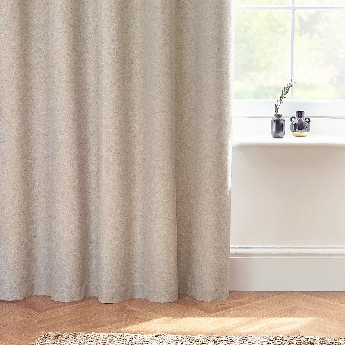 Dawn Linen Reversible Eyelet Curtains in natural marl-effect fabric, shown draped by a window with herringbone flooring and dark vases on the sill.