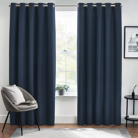 Dawn Plain Lined Eyelet Curtains in midnight blue hanging either side of a window in a living room, with visible eyelet grommets on a metal pole.