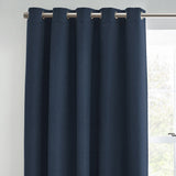 Dawn Plain Lined Eyelet Curtain in midnight blue polyester fabric, shown hanging with silver eyelets on a metal pole beside a window.