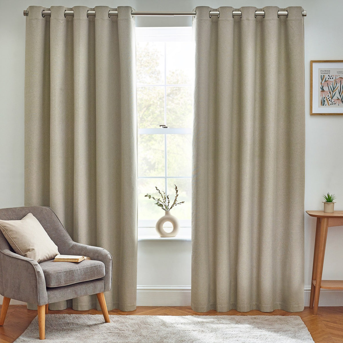 Dawn Plain Reversible Eyelet Curtains in natural marl fabric, shown floor-length on a pole in a living room beside an armchair and window.
