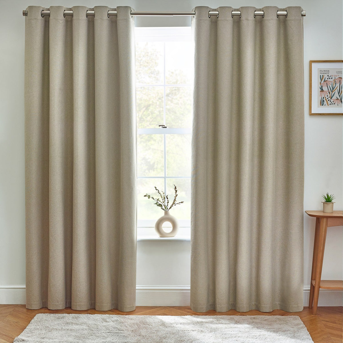 Dawn Plain Reversible Eyelet Curtains in natural marl polyester, shown framing a window in a living room with grommet header, wooden floor, rug, and side table.