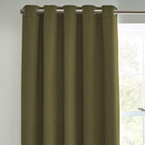 Dawn Plain Lined Eyelet Curtains in olive green fabric with a faintly textured weave, hung from a chrome pole using metal eyelet rings, shown beside a window.