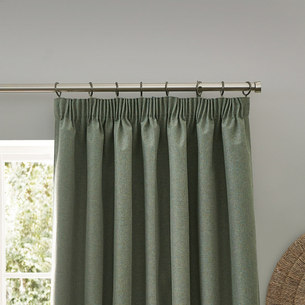 Dawn Reversible Pencil Pleat Curtains in eucalyptus green, showing pleated header hung on a chrome curtain pole with rings against a grey wall.